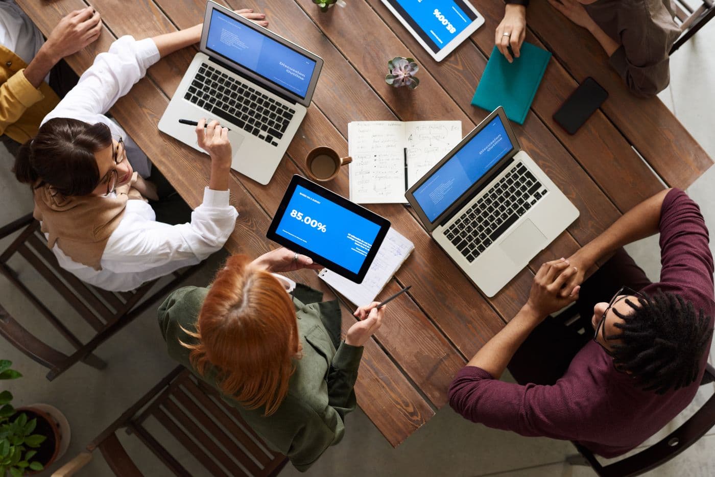 Overhead view of four people collaborating at a shared table with laptops and a notebook