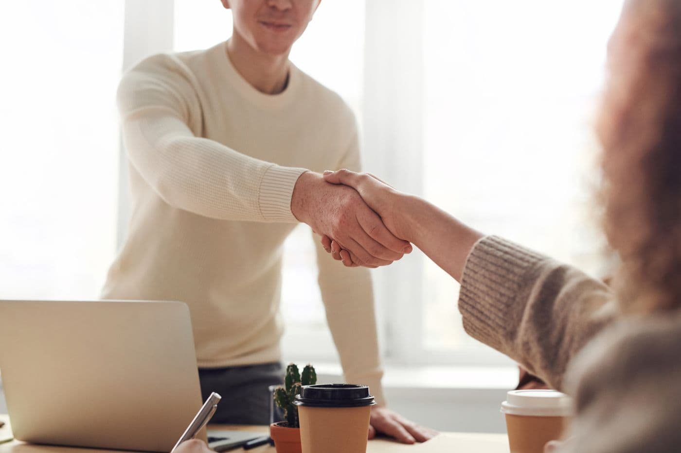 Two people shaking hands across a desk at the start of a meeting