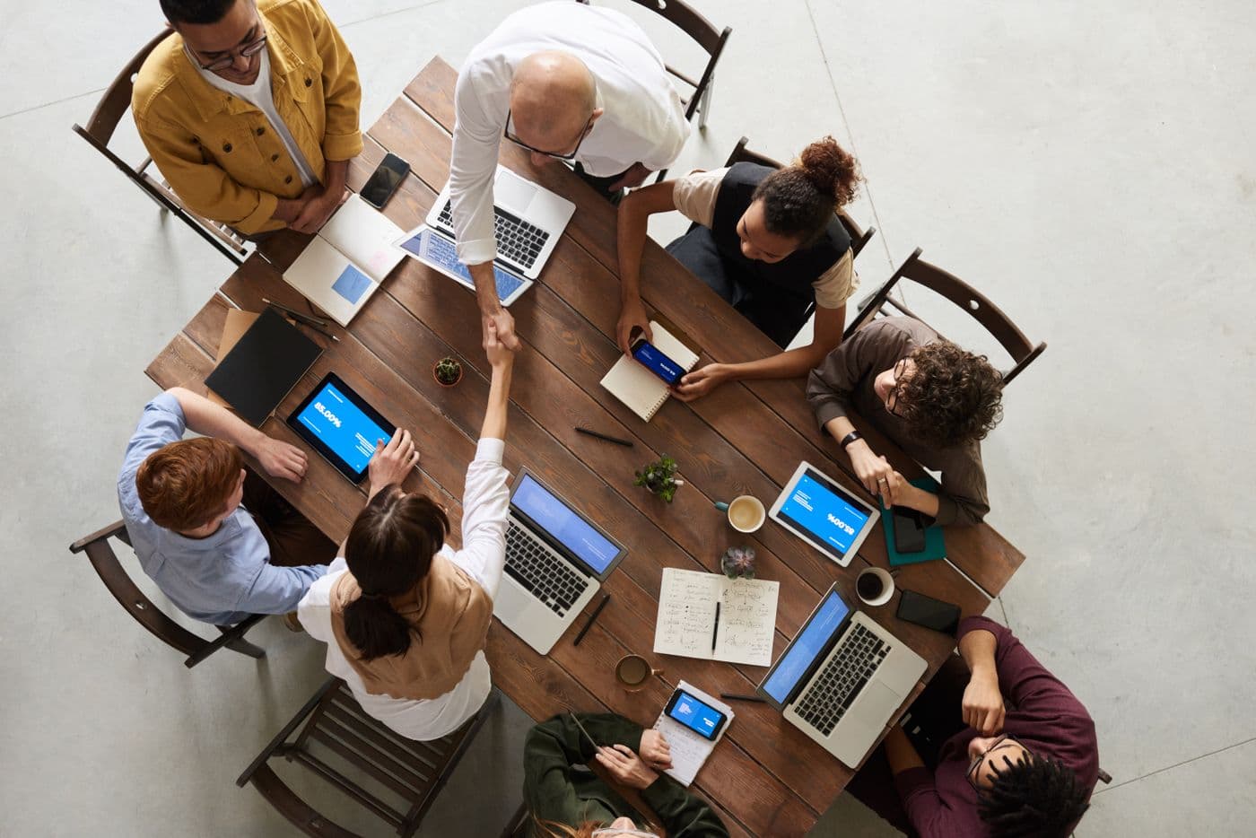 Overhead view of a project team working around a table with laptops, tablets and notes